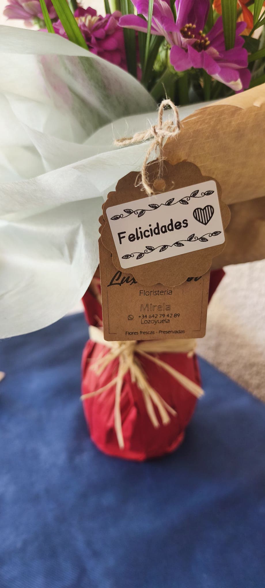Tarjeta de Lux Girasol con el nombre de Mirela atada a un ramo